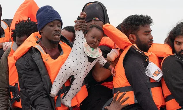 French police stand and watch as months-old baby is carried aboard a packed dinghy headed for Britain